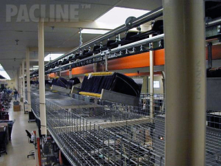 Moving beverage bottle bags from warehouse to assembly onto bottles using enclosed track conveyor system.