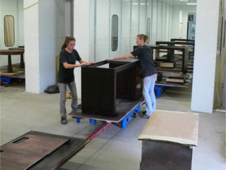 Wooden desks are lightly sanded on towline conveyor system with carts in transit.